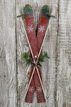 two red skis with snowflakes and evergreen needles on them are hanging from a wooden wall