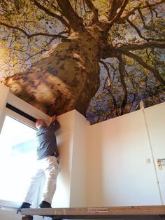 a man standing on top of a ladder in front of a tree painted on the wall