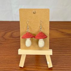 a pair of red and white crocheted mushrooms are displayed on a wooden stand