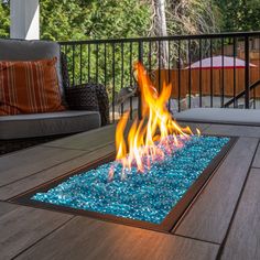 an outdoor fire pit on a deck with chairs and umbrellas in the back ground