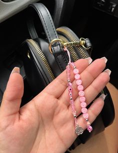 a woman holding two pink beads in her hand and a black purse behind her on the floor