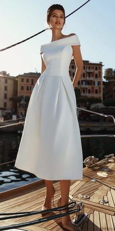 a woman in a white dress standing on the deck of a sailboat with buildings in the background