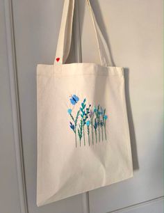 a tote bag hanging on a door with blue flowers painted on the front and side