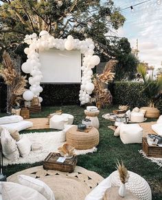 an outdoor movie party with white balloons and pillows on the grass in front of a large screen