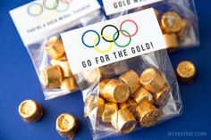 some gold coins are sitting in plastic bags on a blue surface with the olympic logo