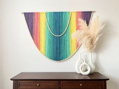 a wooden dresser topped with a white vase filled with flowers and a rainbow wall hanging