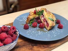 a blue plate topped with raspberries next to a bowl of raspberries