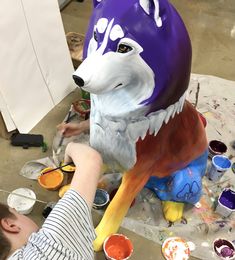 a person painting a large purple and white animal