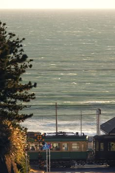 the train is going down the tracks by the water's edge with power lines above it