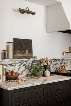 a kitchen with marble counter tops and black cabinets, an art piece on the wall