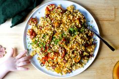 a white plate topped with corn and vegetables next to a child's hand on the table