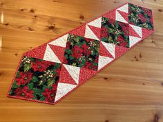 a red and white quilted table runner with poinsettis, holly and berries