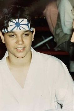 a young man wearing a blue and white headband with an evil look on his face