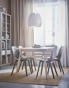 a dining room table and chairs in front of a large window with white drapes