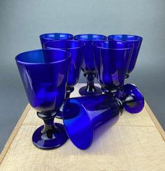 six blue glass goblets sitting on top of a wooden table next to each other