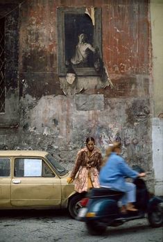 a man and woman on a moped in front of a building with a painting