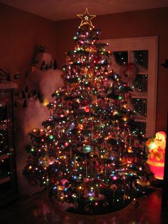 a brightly lit christmas tree in the corner of a room with other decorations and lights