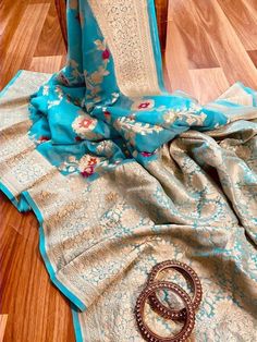 This is a pure khaddi georgette banarasi saree in light blue color with meenakari and golden zari weave. Saree features a contemporary and spacial floral jaal using vibrant colors and golden zari in the body of the saree. Golden zari floral motif with floral jaal is intricately woven in the pallu, the pallu is finished with ultra-fine tassels in multicolor. Paisleys and floral design in a structural pattern are compactly woven in the border of the saree. This is paired with a plain blouse with a Elegant Blue Saree With Meenakari Details, Sky Blue Banarasi Saree, Meenakari Semi-stitched Banarasi Silk Saree, Blue Meenakari Semi-stitched Saree, Saree Golden, Pure Georgette Banarasi Saree, Khaddi Georgette Banarasi Saree, Georgette Banarasi Saree, Banarsi Saree