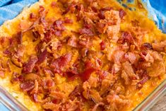 a casserole dish with bacon and cheese in it on a blue cloth next to a wooden table