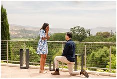 a man kneeling down next to a woman talking on a cell phone while standing near a railing