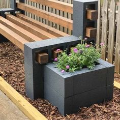 a wooden bench sitting next to a planter filled with flowers on top of mulch