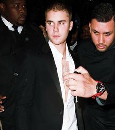 a man in a black suit and white shirt standing next to another man with a watch on his wrist