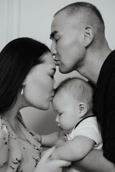 a man and woman kissing their baby while he holds the baby's head in front of them