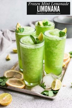 three glasses filled with green liquid and garnished with lemons, mint and lime slices