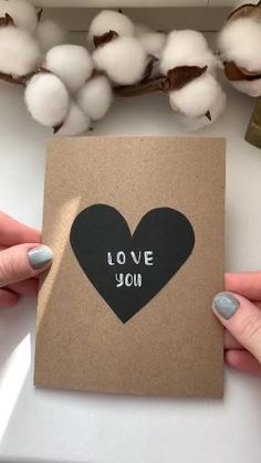 two hands holding a card with the words love you on it and a cotton plant in the background