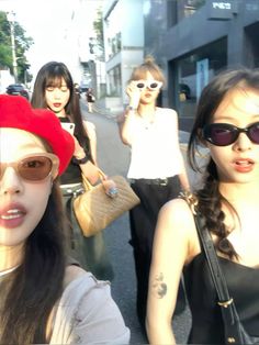 three women walking down the street with one holding a cell phone to her ear and wearing sunglasses