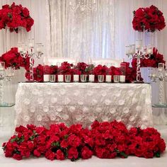 a table topped with lots of red flowers next to tall vases filled with roses