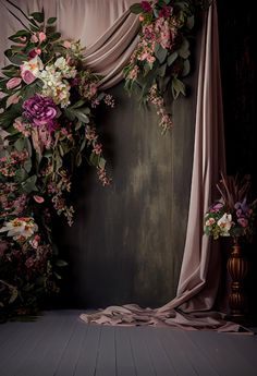 an arrangement of flowers and greenery in front of a drapeed curtain on a wooden floor