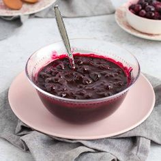 a bowl filled with blueberry sauce on top of a pink plate next to other plates