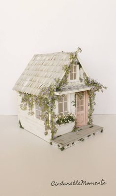 a doll house with ivy growing on the roof and windows, in front of a white wall