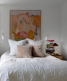 a bed with white sheets and pillows next to a painting on the wall above it