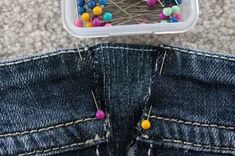 a pair of jeans with pins in them and a plastic container on the floor next to it