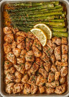 chicken and asparagus in a pan with lemon wedges