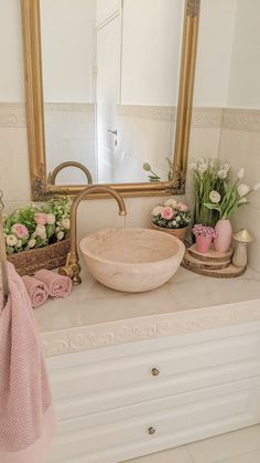 a bathroom sink sitting under a large mirror next to a wooden basket filled with flowers