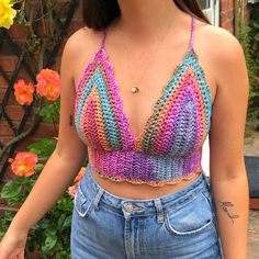 a woman wearing a crochet top and jeans in front of flowers with her hand on her hip