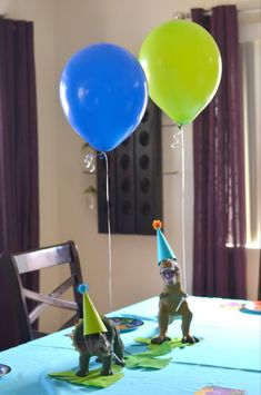 two balloons are on the table and one balloon is in the shape of a dinosaur