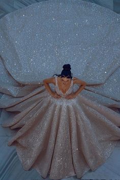 a woman laying on top of a white bed covered in glittery fabric and wearing a dress