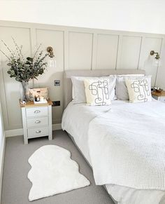 a white bed sitting in a bedroom next to a nightstand with a vase on it