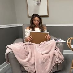 a woman sitting in a chair under a blanket on top of a table with a tablet