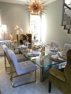 a dining room table with white chairs and a chandelier above it in front of a staircase