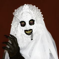 a woman dressed as a ghost with black makeup and white dress holding her hand up