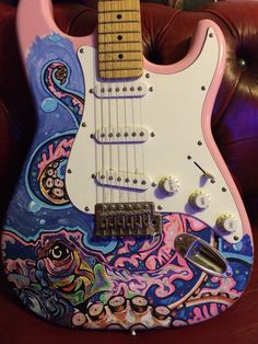 a pink and blue guitar sitting on top of a couch