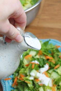 a person pouring dressing into a salad on a blue plate with lettuce and carrots