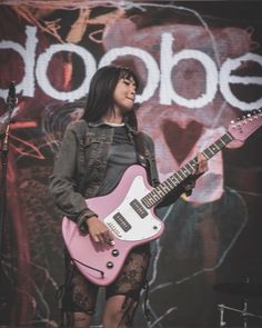 a woman holding a pink guitar while standing in front of a microphone and stage sign