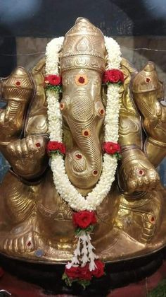 an elephant statue with flowers around it's neck and head on display in a glass case