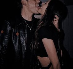 two people standing next to each other in a dark room with one person kissing the other